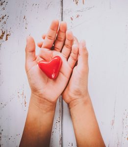 Image of 2 hands holding a red heart shaped stone