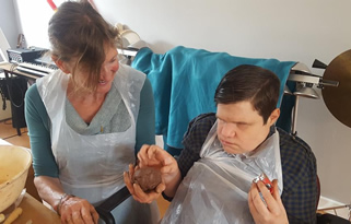 Staff and service user sitting side by side and shaping clay with their hands during a pottery activity
