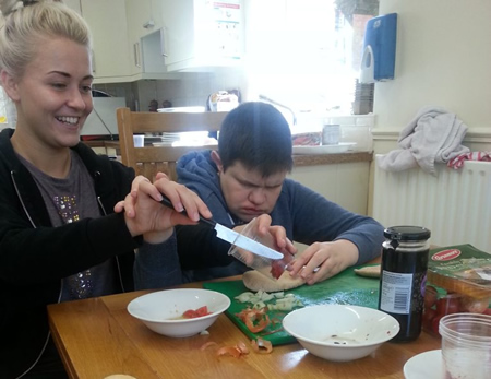 Image of staff and service user sitting side by side chopping veg in kitchen