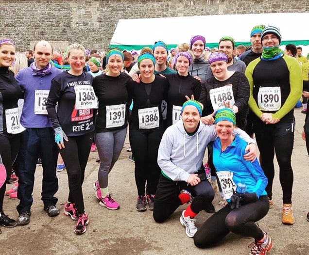 Image of 16 staff members from the Anne Sullivan Centre posing after completing Runamuck Challenge in Coolcarrigan Estate, Coill Dubh, Co Kildare. They are wearing running gear and contestant numbers.