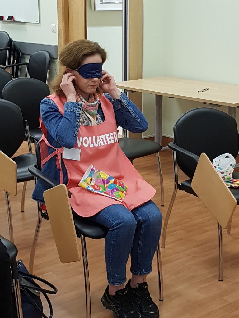 person sitting down putting on blindfold and earplugs during deafblind awareness session
