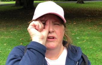 Picture of Susan in a park, she is wearing a pink cap and has her hand in front of her eye to show what her eyes can see