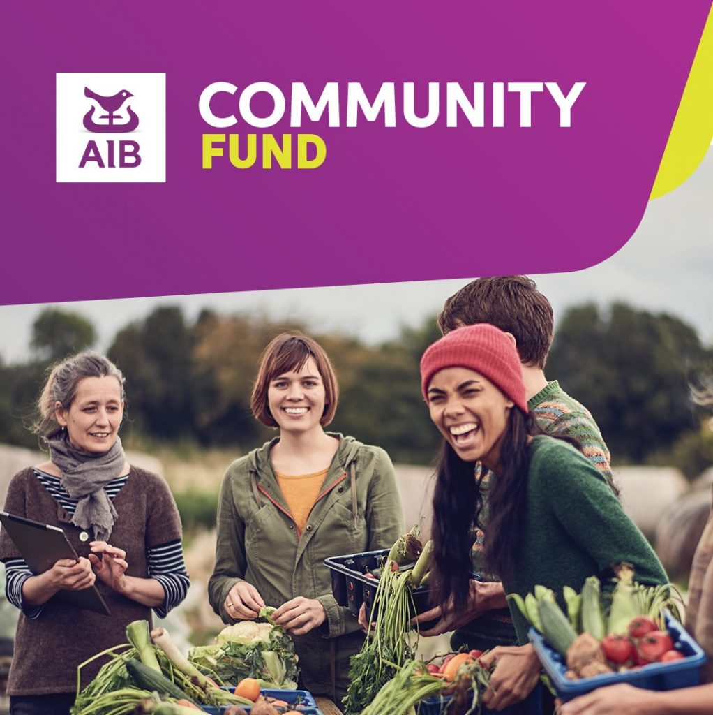 AIB logo and the words community fund above photo of 4 people smiling and laughing outdoors carrying vegetable baskets